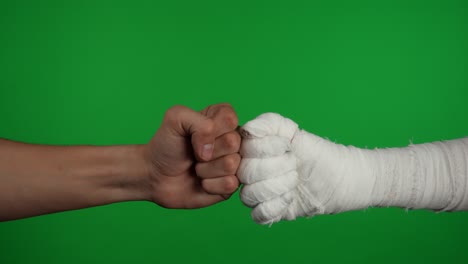 two fists, one bandaged, bumping each other on a green screen