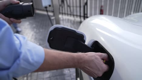 el hombre de negocios conecta el enchufe del cargador progresivo de la estación de carga a su ev.