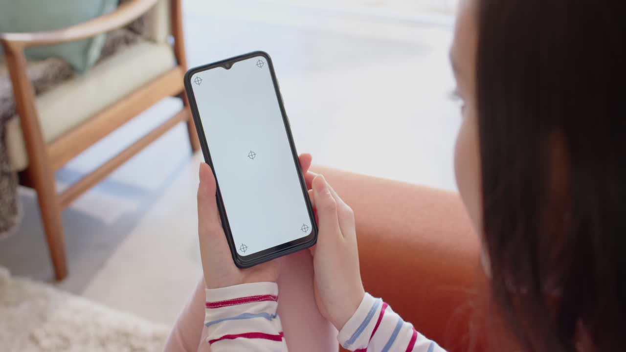 Mujer sentada en el sofá de casa sosteniendo un smartphone con la pantalla en blanco.