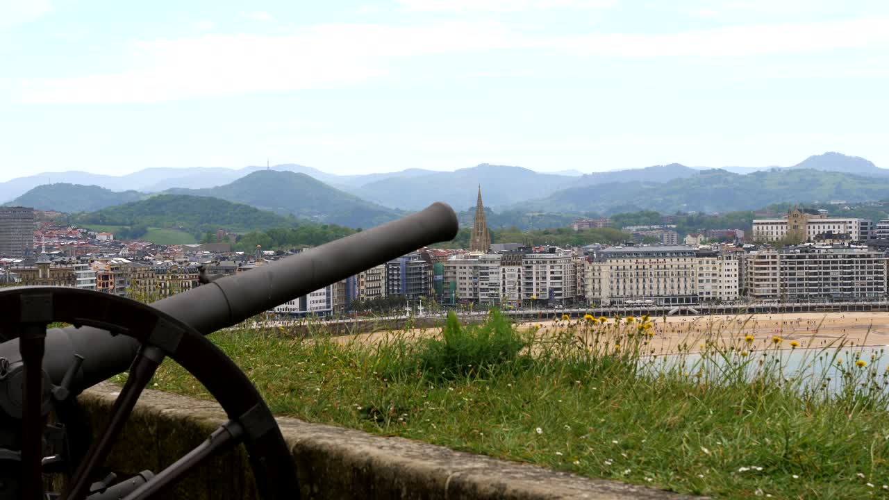 Close up shot of historic artillery gun on urgull mountain with sandy beach and skyline of San Sebasti&aacute;n in background