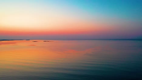 Leuchtend-Orangefarbener-Sonnenaufgang-Am-Meer-Mit-Farben,-Die-Sich-über-Den-Plätschernden-Wasserwellen-Spiegeln