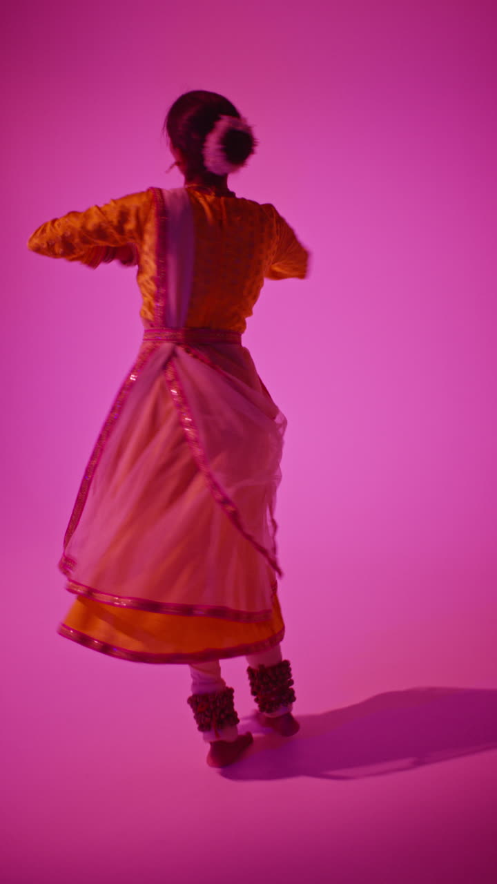 video vertical de larga duración en estudio de una bailarina de kathak que realiza un baile vestida con el vestido tradicional indio contra un fondo púrpura 3