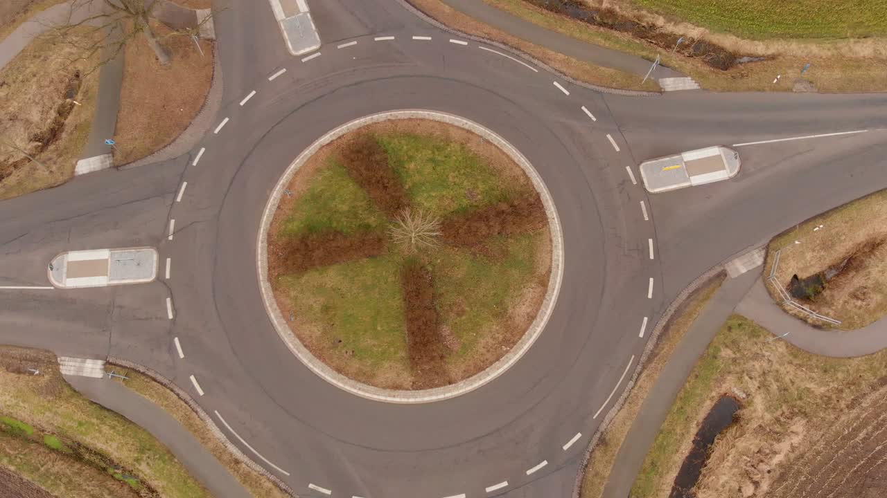 vuelo circular con vista aérea de una pequeña rotonda en la intersección de dos carreteras de campo grises asfaltadas en el norte de alemania
