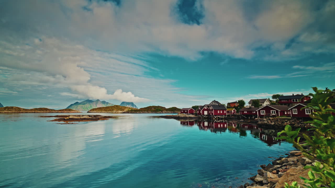 Picturesque nordic landscape. Lofoten islands, Norway.
Blue cloudy sky reflecting on the still sea. View of the red fishermen cabins.