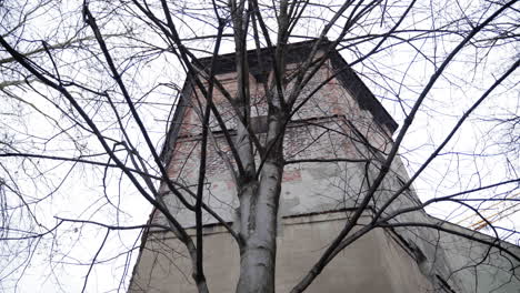 a historic medieval watchtower in munich, germany, partially obscured by leafless trees. the overcast sky and aged brick structure create a moody, winter atmosphere.