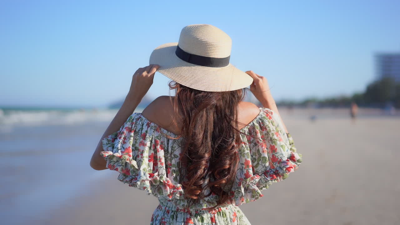 Back of Female With Long Hair With Summer Hat and Dress Standing Alone on Beach on Sunny Summer Day