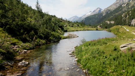 aerial view moving forward from a river to the mountain lake of turquoise clear water, in the summer