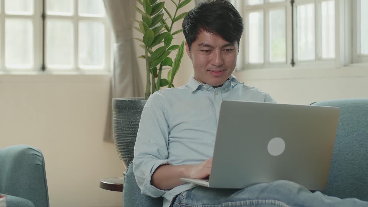 Male Use Laptop Computer And Smiling In Living Room While Lying On Sofa, Video In 4K
