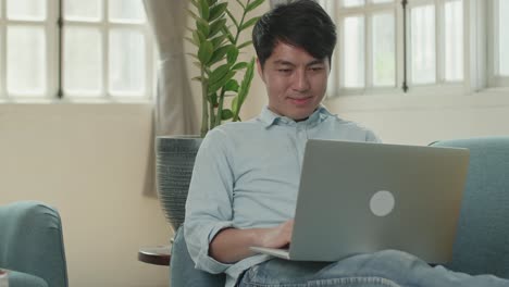 male use laptop computer and smiling in living room while lying on sofa, video in 4k