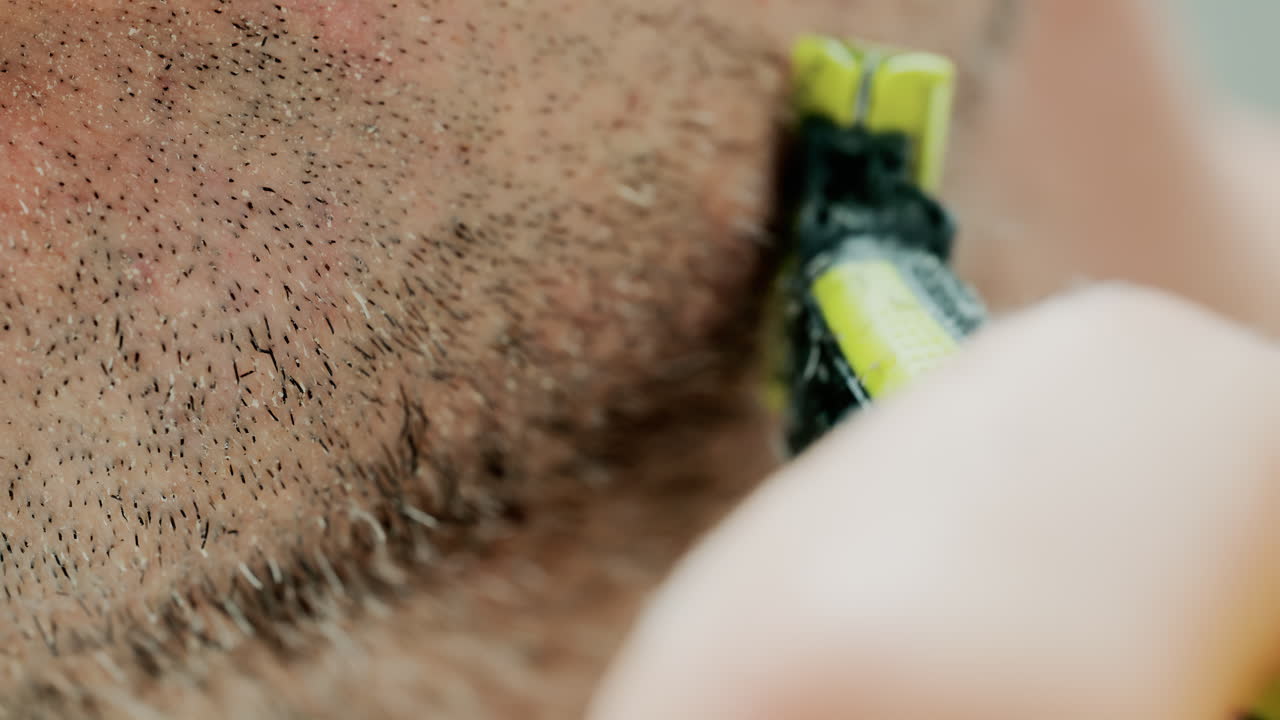 Close up of a man using an electric razor to trim facial hair in the bathroom