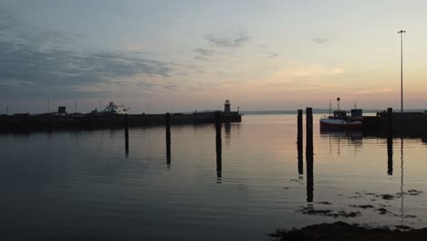 aerial view flying towards silhouette small lighthouse between broken wooden jetty beams at sunrise