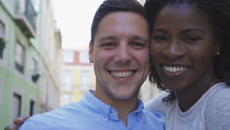 una pareja de jóvenes multirraciales sonrientes posando para una selfie al aire libre.