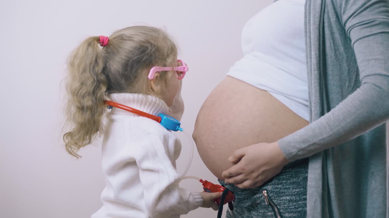 un niño con un estetoscopio de juguete escucha a una mamá embarazada en la habitación