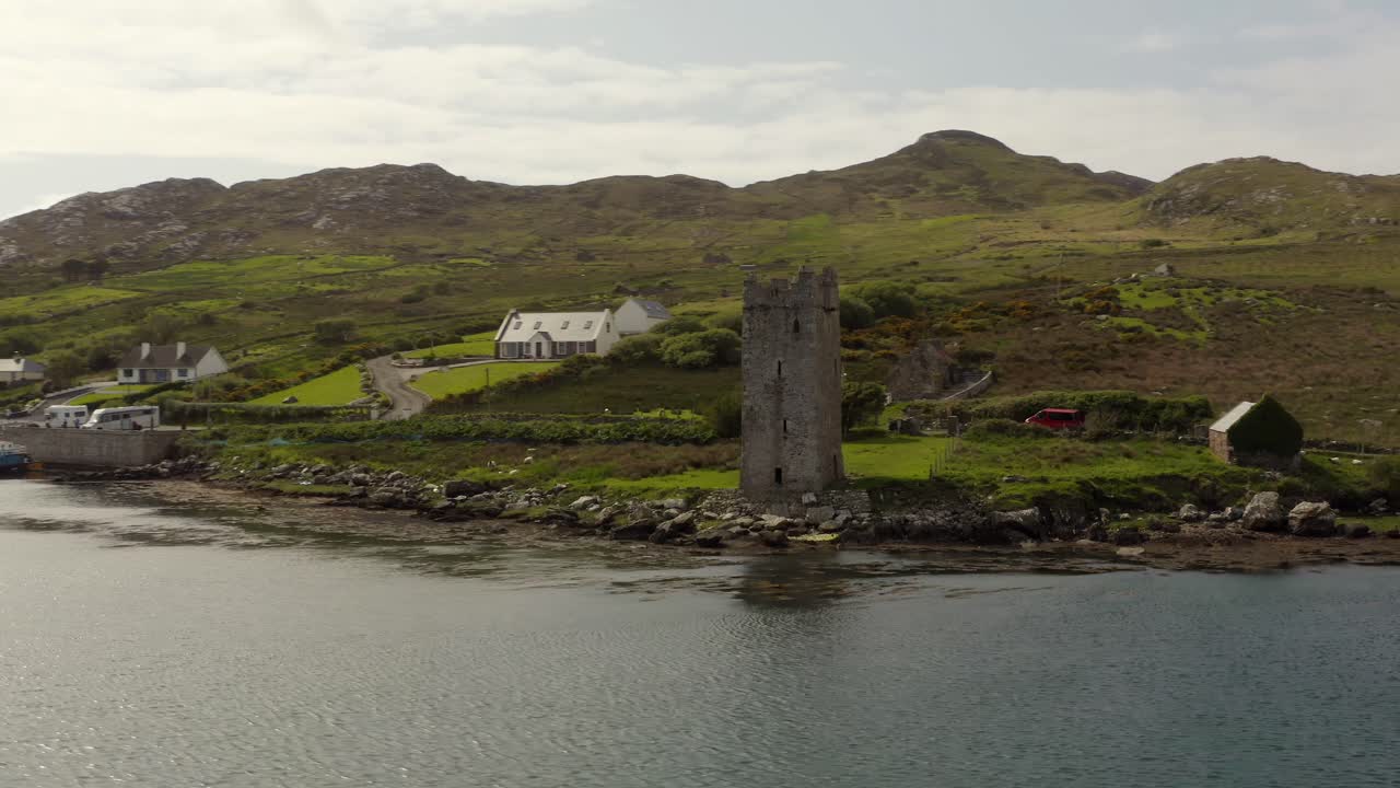 Aerial parallax around Grace O'Malley's Towerhouse fronting grassy green hillside, cloudy day