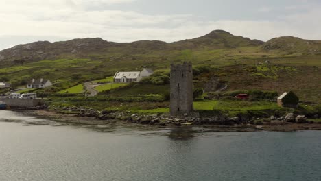 aerial parallax around grace o'malley's towerhouse fronting grassy green hillside, cloudy day