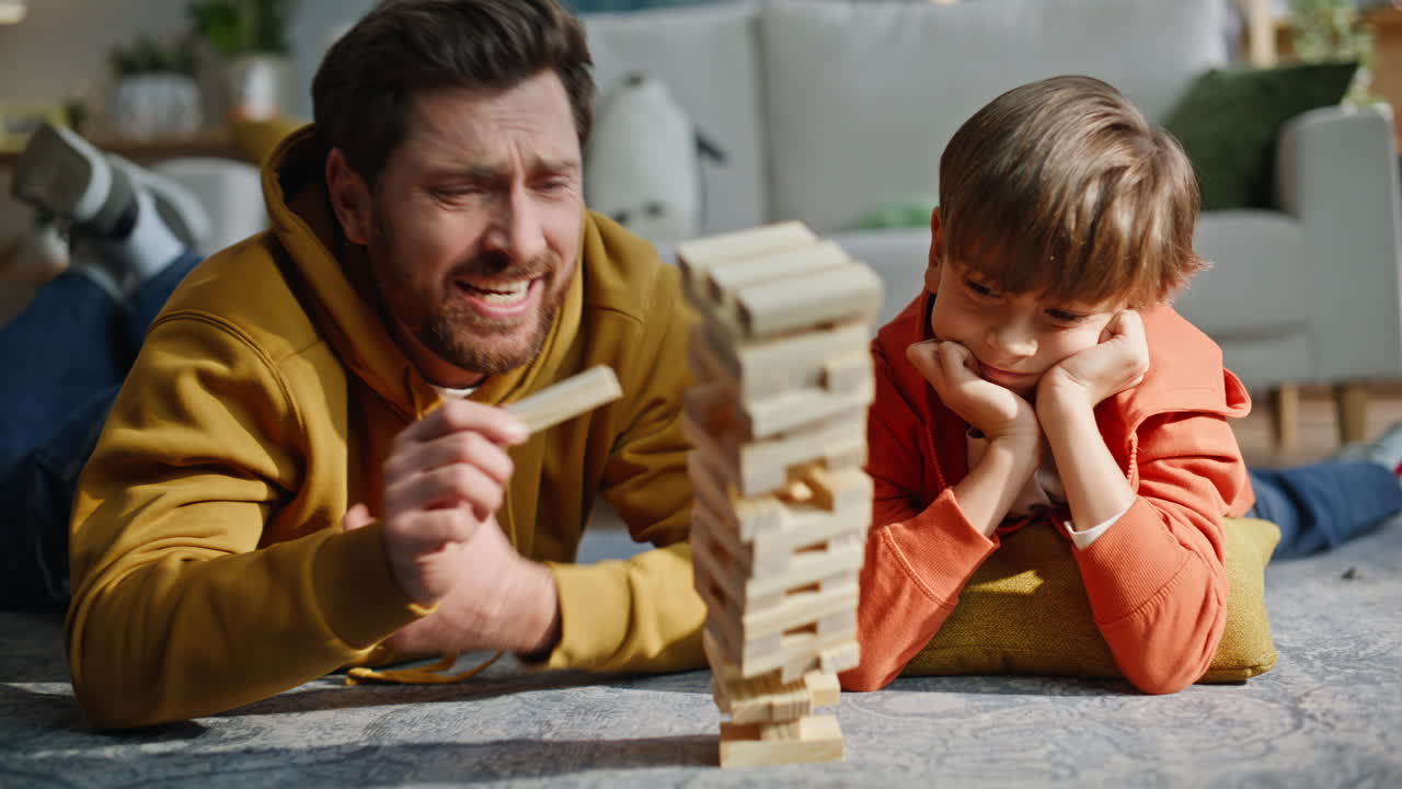 Primo piano di uomo che estrae un blocco di Jenga rovinando la torre di legno, provando frustrazione a casa.