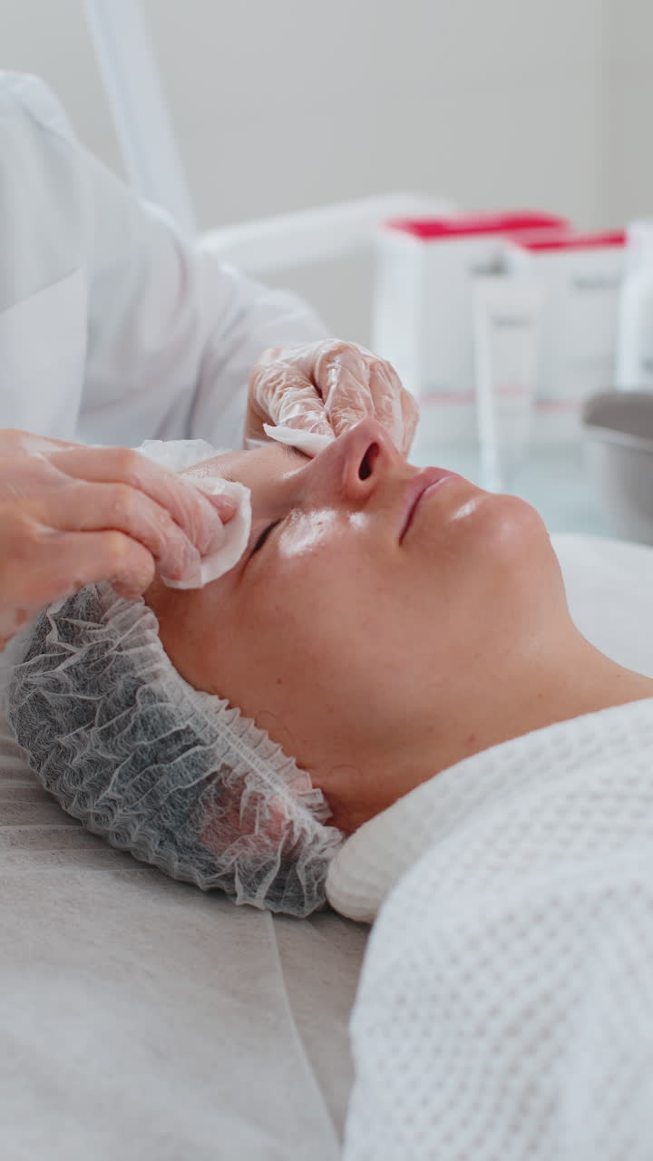 Medico estetico che deterge il viso e gli occhi di una donna con dischetti di cotone durante una procedura di pulizia in una clinica estetica.