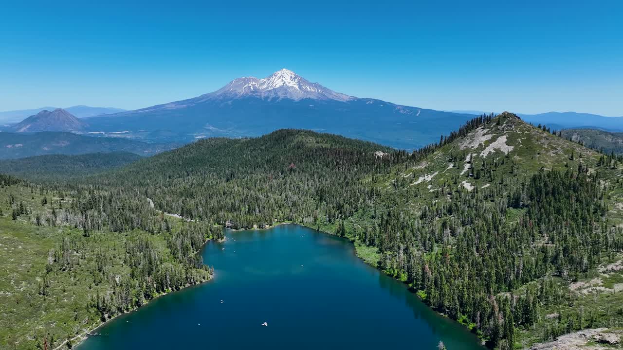 Flying low to the ground over a ridge towards snow-capped Mount Shasta in California to dramatically reveal the crystal clear glacial waters of Castle Lake