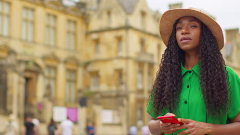 female tourist on vacation in oxford uk exploring city walking along broad street using mobile phone for directions and information