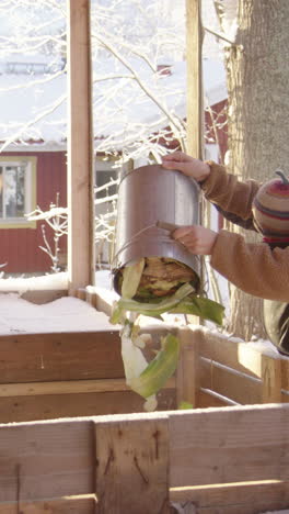 a mother with child in sling empties compost bucket in a snowy scene, vertical