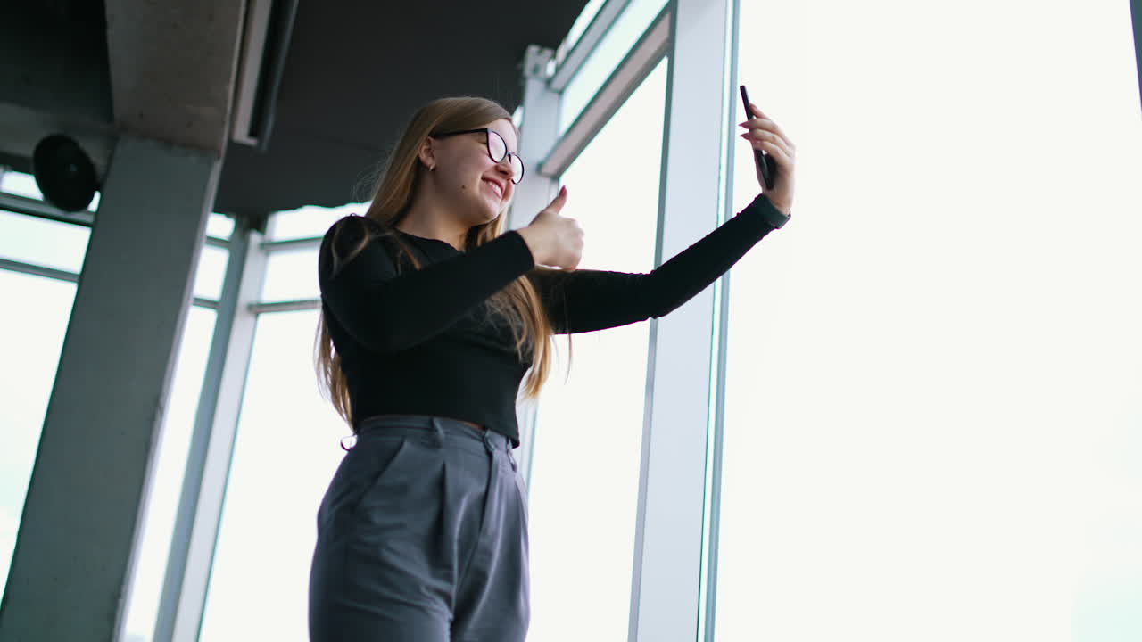 Happy female freelancer in formal wear with eyeglasses taking selfie on cellphone