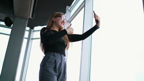 happy female freelancer in formal wear with eyeglasses taking selfie on cellphone