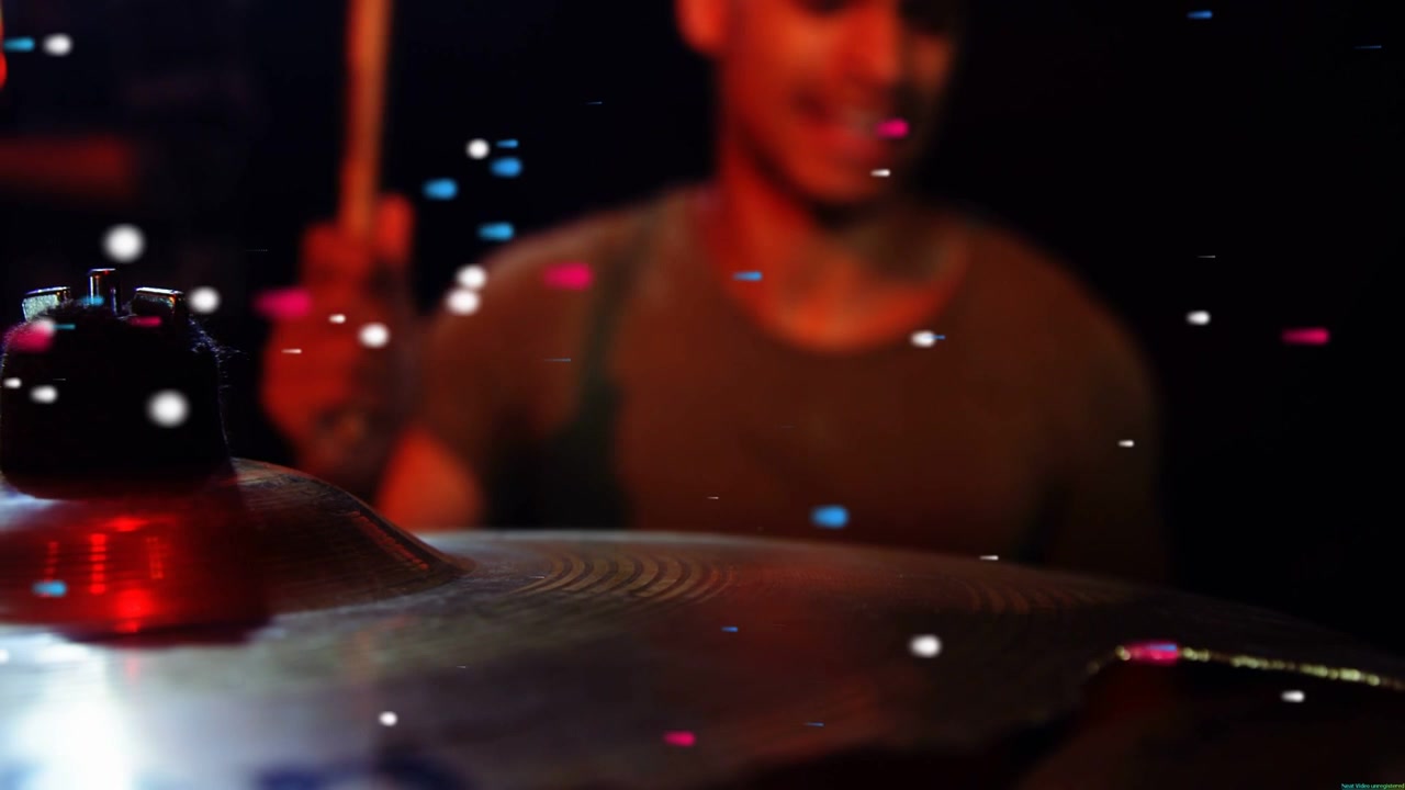 Drummer striking cymbal with drumstick entering frame for music, particles drifting across kit