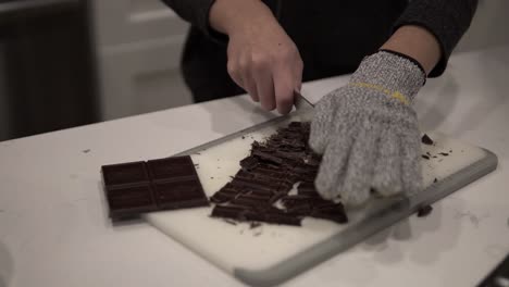 a young girl cuts up dark chocolate before melting it for millionaire shortbread cookies while wearing safety gloves-6