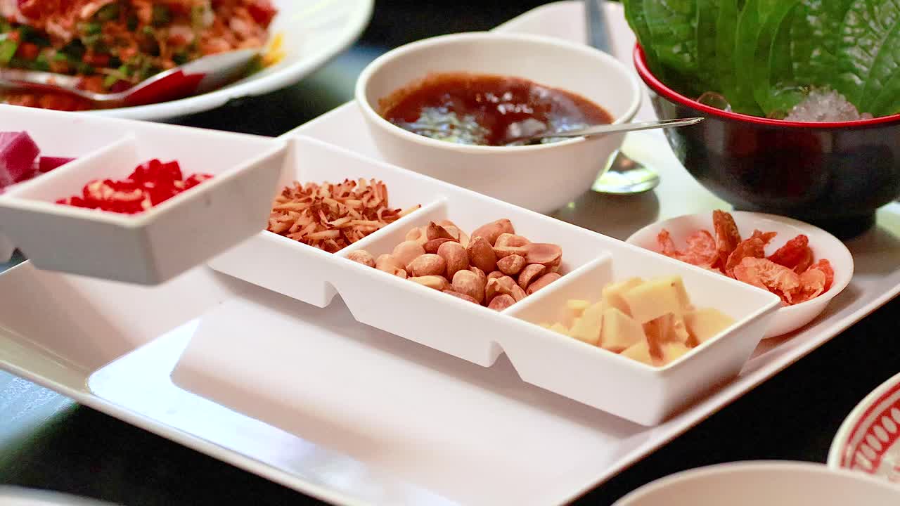 Hands arranging ingredients for Miang Kham on a tray. Bright lighting highlights vibrant colors and textures in a Thai culinary setting