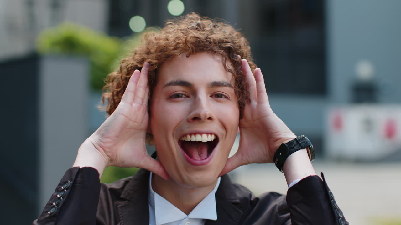 Businessman looking at camera shocked by sudden victory game winning good news outside office