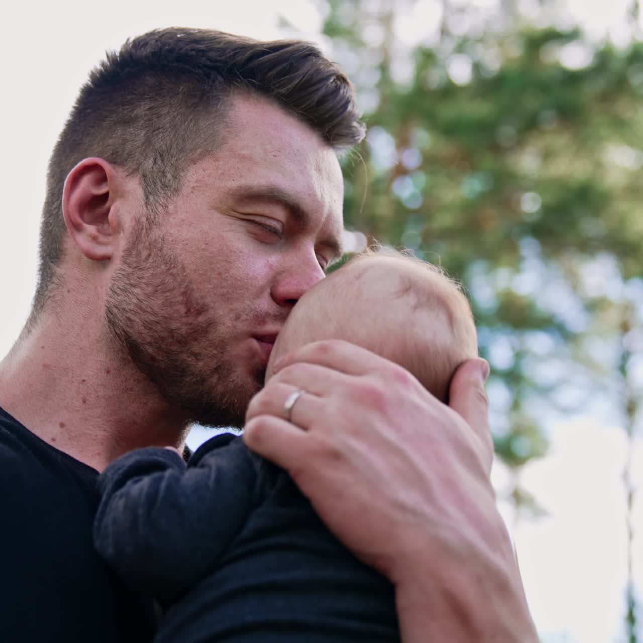 Uomo caucasico muscoloso e barbuto che tiene in braccio il suo neonato. Un papà affettuoso bacia teneramente il suo amato figlio.