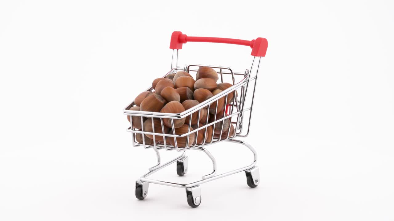 Shopping cart filled with hazelnuts rotating on the turntable. Isolated on the white background. Close-up.
