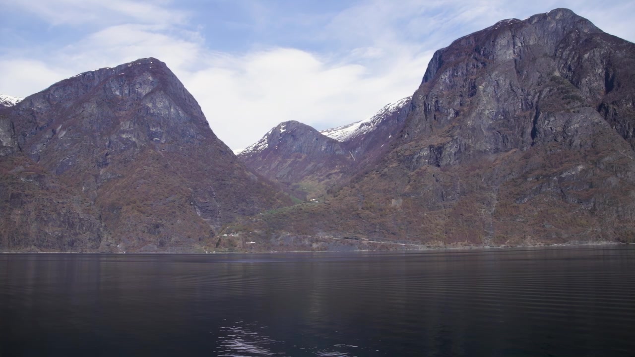 Stille fjordvand reflekterer stejle bjerge under en delvist overskyet forårshimmel i Norge