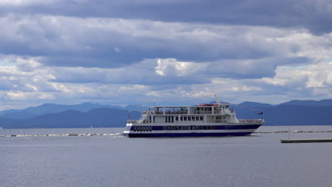 a riverboat tour gets underway under an overcast sky with mountains