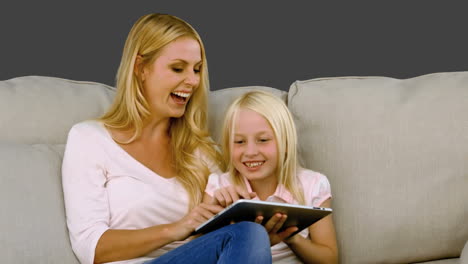 mother and her daughter using digital tablet on sofa in slow motion