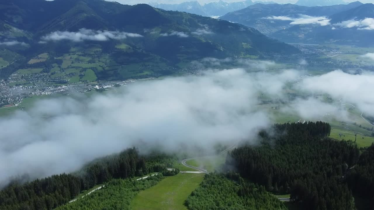 volando sobre una pista de esquí en verano en los alpes con nubes bajas sobre el pueblo de abajo