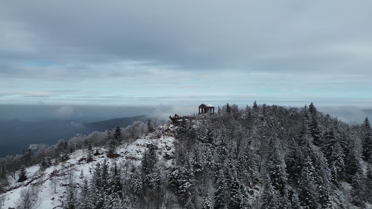 Drone footage of Temple du Donon covered in snow, perched on a mountain top with breathtaking winter views."