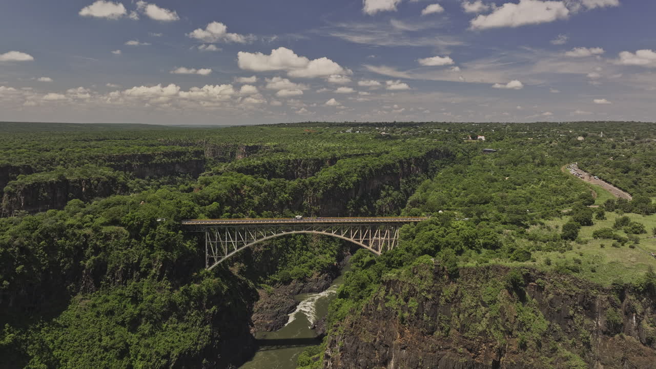 Sobrevoo aéreo v7 das Cataratas Vitória, Zimbábue, capturando a histórica ponte em arco que atravessa o Rio Zambeze entre as cidades, rodeada por uma paisagem natural exuberante - Filmado com Mavic 3 Pro Cine - 3 de janeiro de 2024.