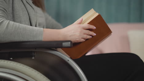 Manos-De-Mujer-En-Silla-De-Ruedas-Hojeando-Páginas-De-Un-Libro-Marrón