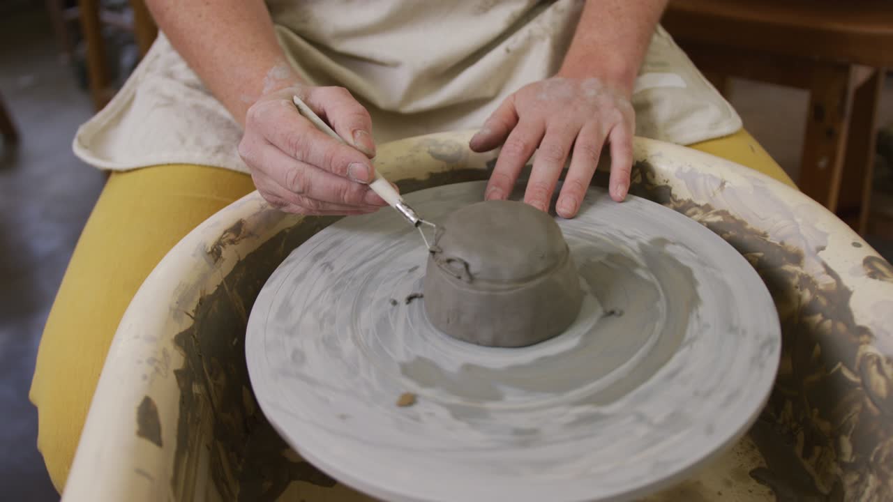도자기 스튜디오에서 도자기를 마무리하기 위해 루프 도구를 사용하는 여성 도자기의 중간 섹션