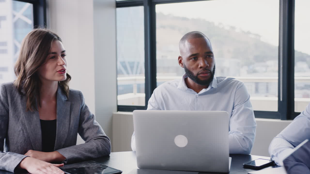 Corporate business colleagues sitting around a table in a meeting room talking, arc shot, close up