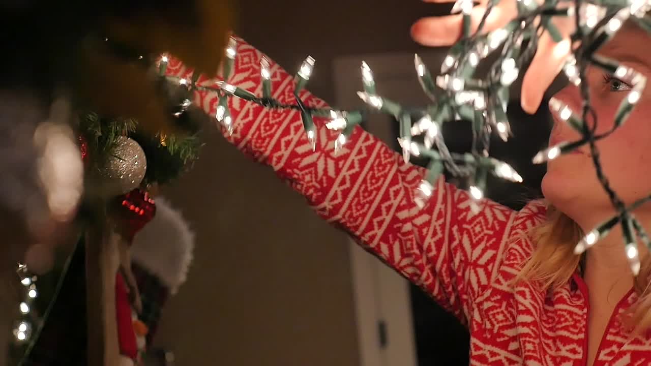 jovencita colgando luces navideñas en el manto