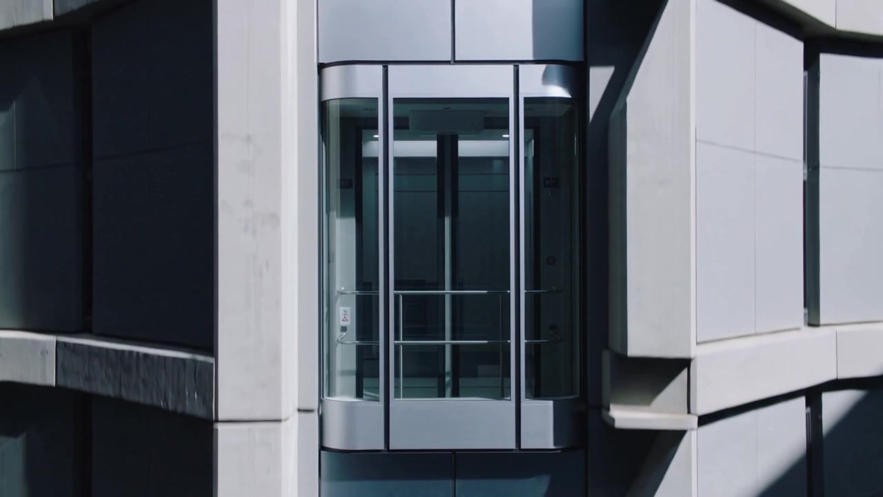 Rising glass panoramic elevator cabin on concrete facade, motor starting, showing handrail