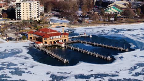 drone orbits above boathouse pier on frozen lake geneva during cold winter day
