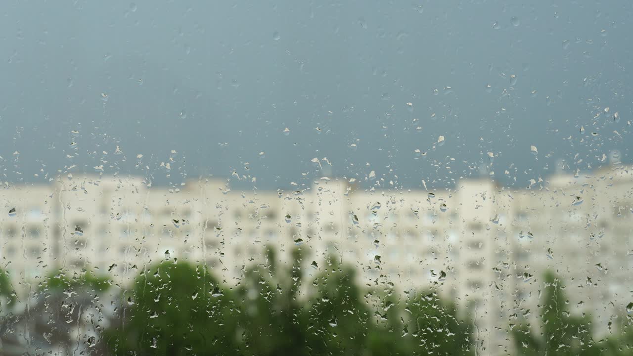 창문 유리 위에 물방울, 도시에서 여름 비, 파란 하늘, 집과 푸른 나무의 흐릿한 실루, 4k 비디오