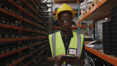 trabajador de fábrica afroamericano en una fábrica con un chaleco de alta visibilidad usando una tableta