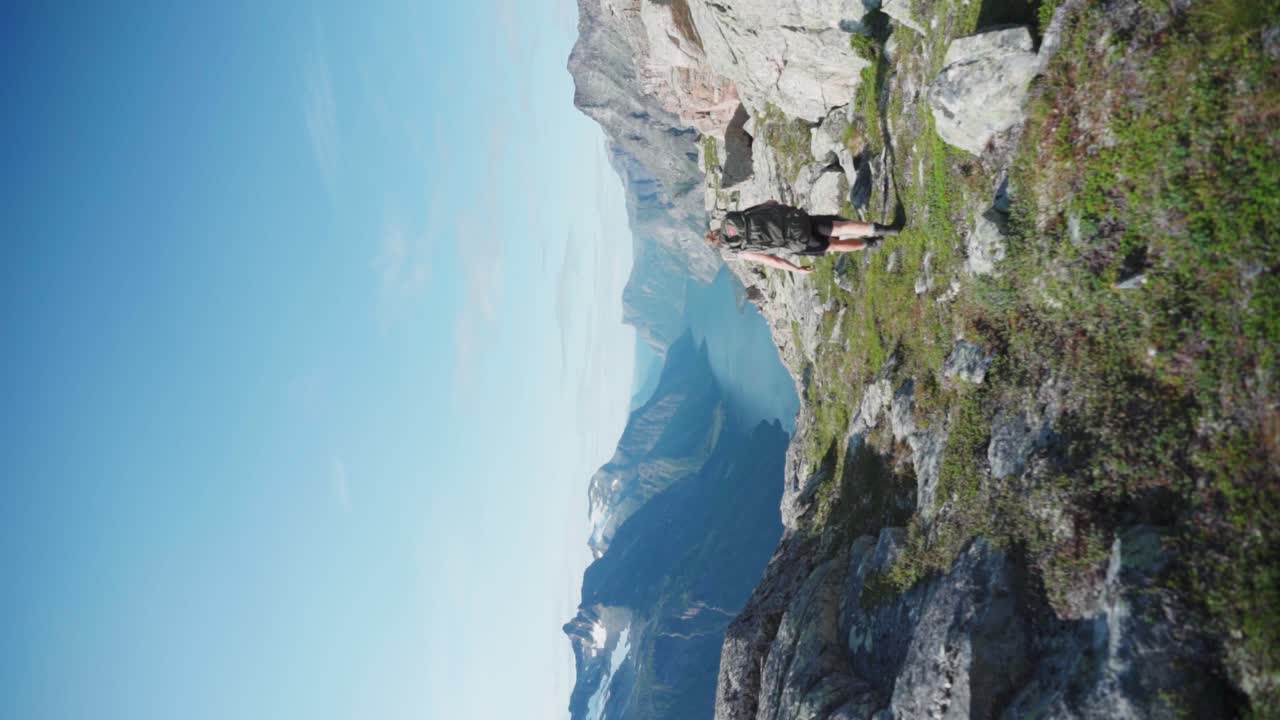 Scatto verticale di un escursionista e un cane che scalano una montagna rocciosa che offre una vista maestosa sul lago in estate