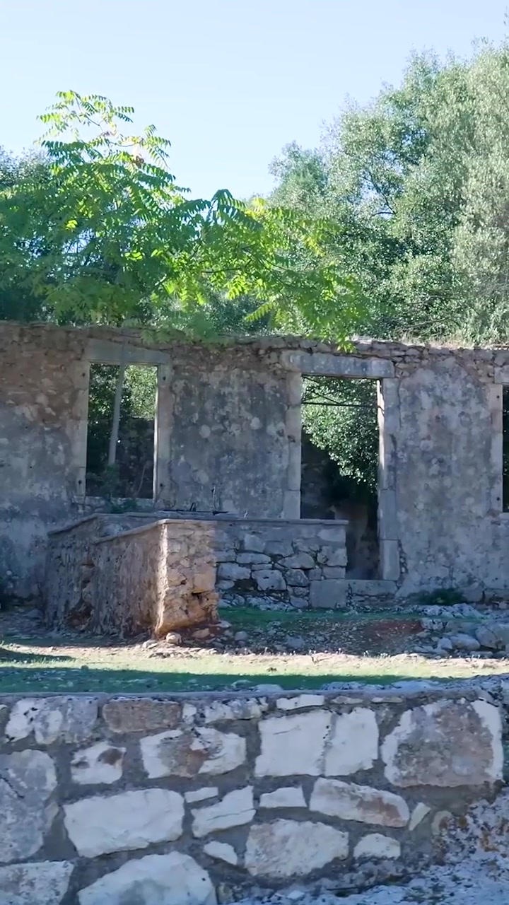 Vista de las ruinas de piedra de una casa abandonada en el antiguo pueblo de Valsamata con vanos de puertas y ventanas vacíos, rodeada de vegetación y luz solar en Cefalonia, Grecia