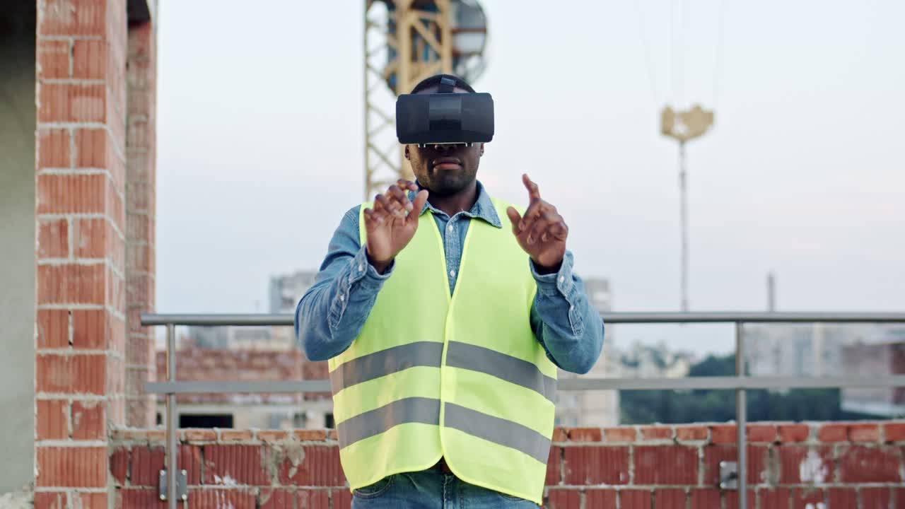 African American man architect or foreman in VR glasses standing on the roof at the building site and having headset as watching virtual tour of future architecture. Outdoors. New modern technologies.