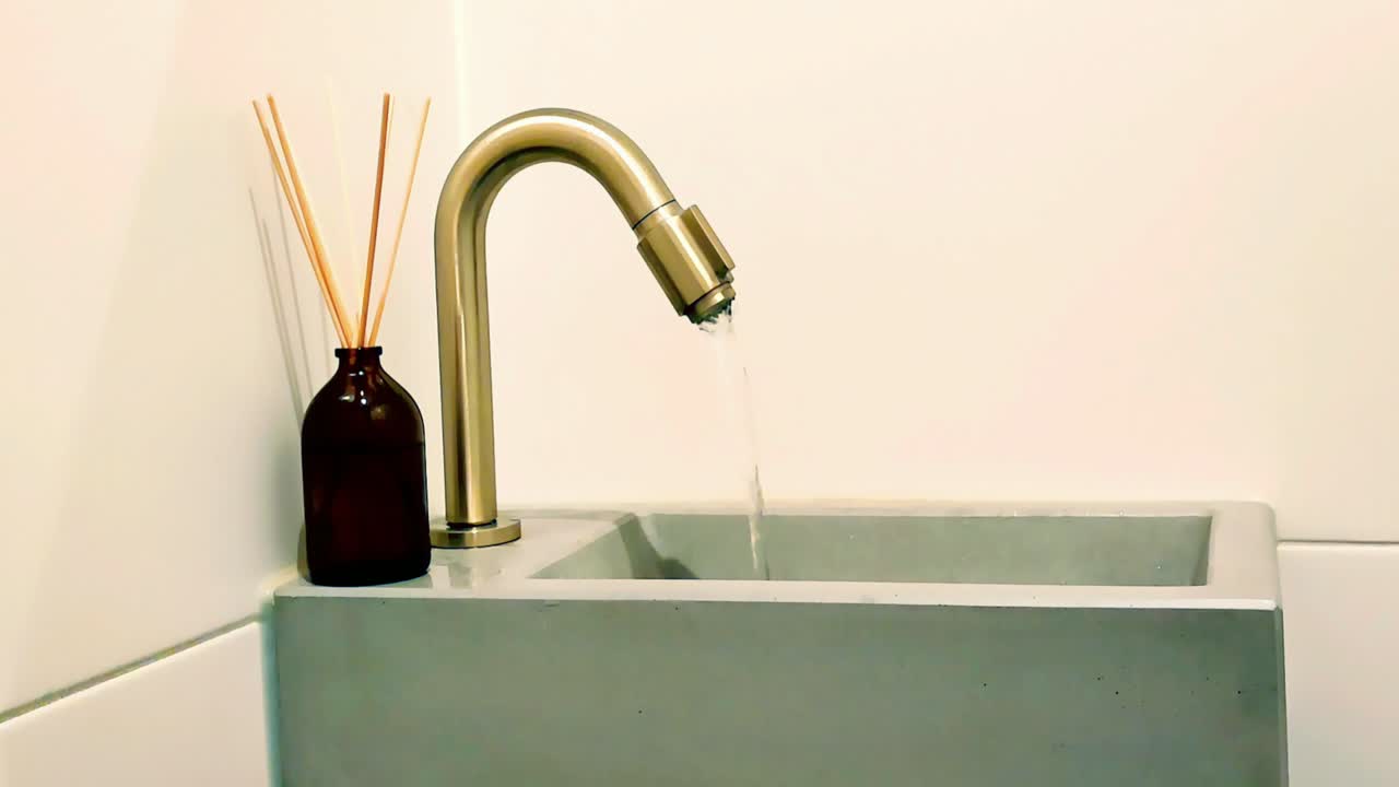 Running tap water out of a golden toilet faucet draining in a concrete sink